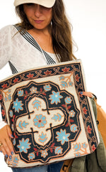 Woman holding a large, intricately designed bag with floral patterns.